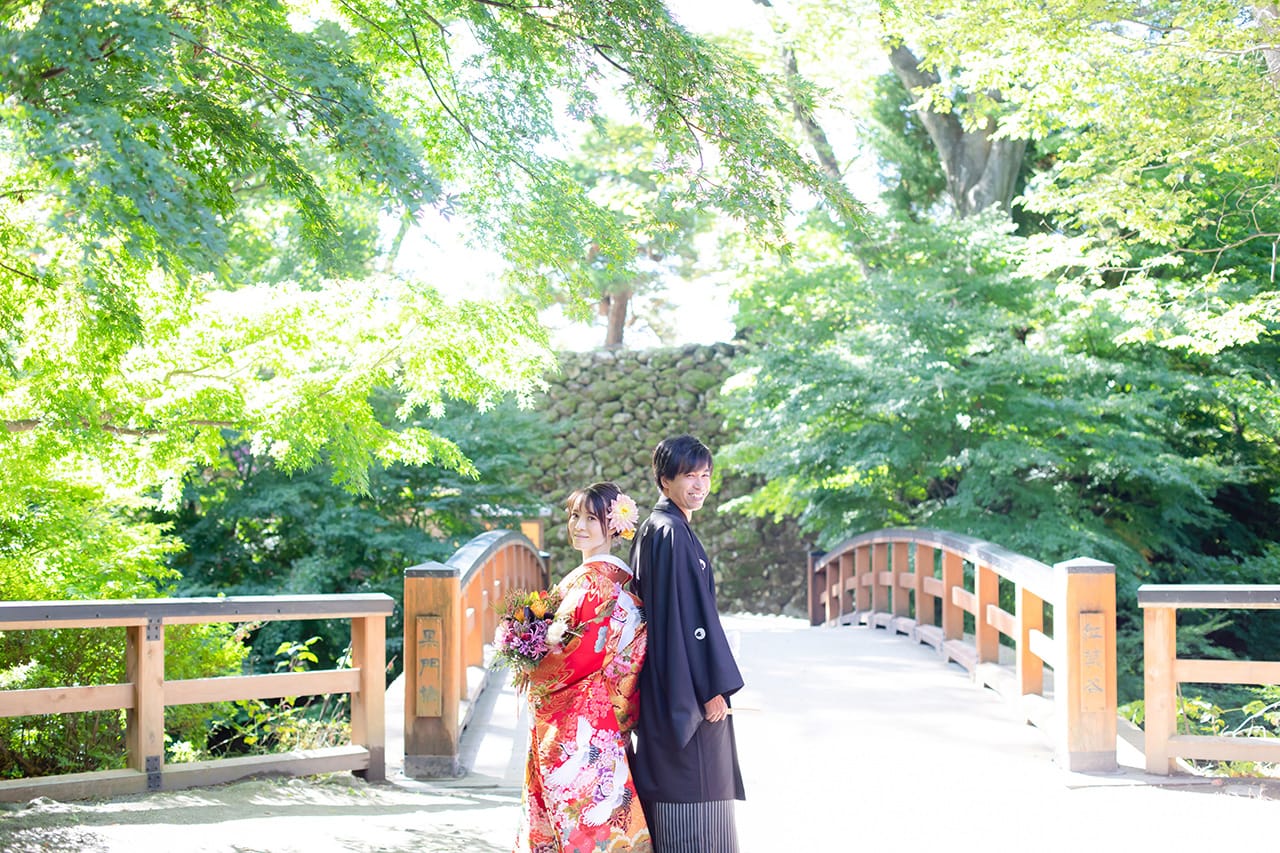 伝統的な木造の橋の前で微笑む和装のカップル